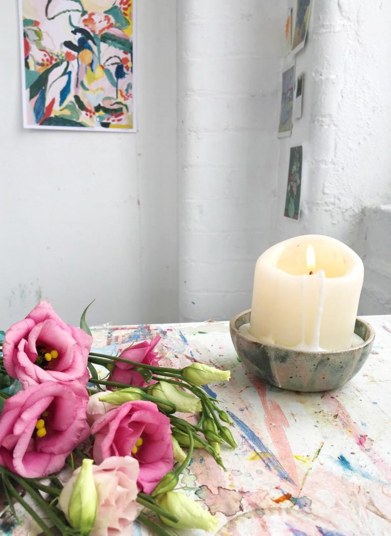 Laura lights a candle and works on her paint-splattered desk